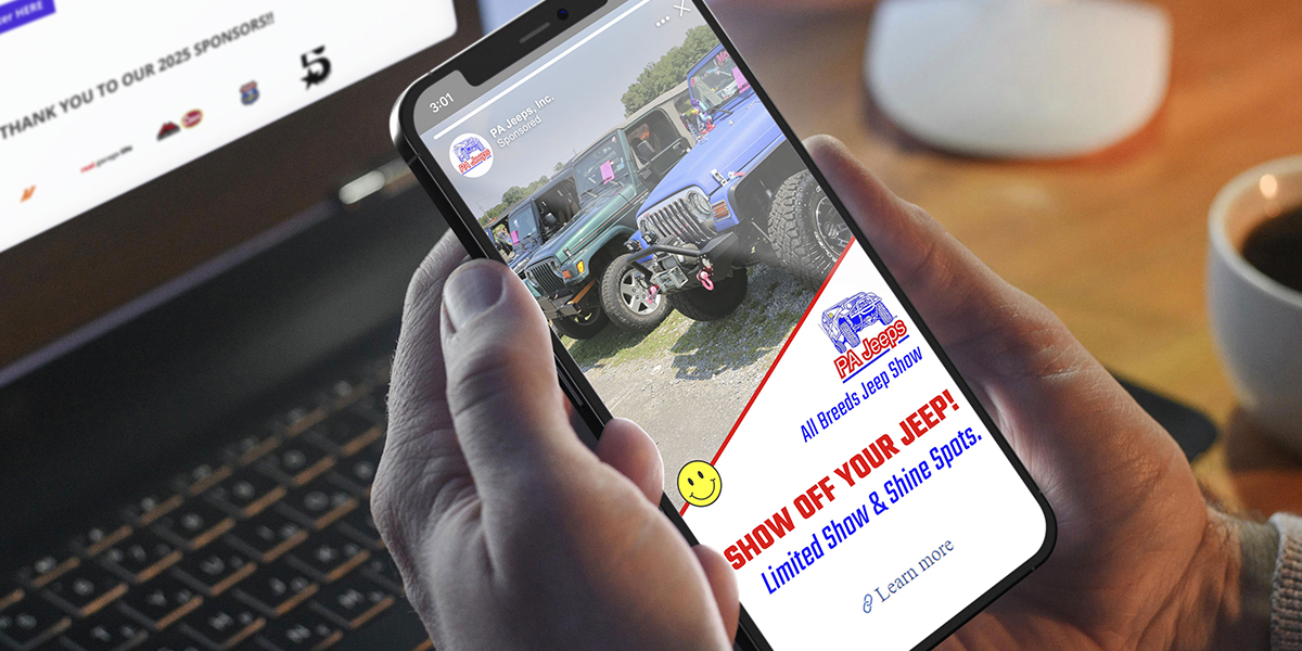 A person holds a smartphone displaying a Jeep event promotion, with a laptop and coffee cup visible in the background.